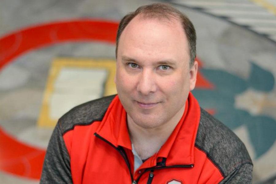 man in scarlet and gray in front of university floor seal