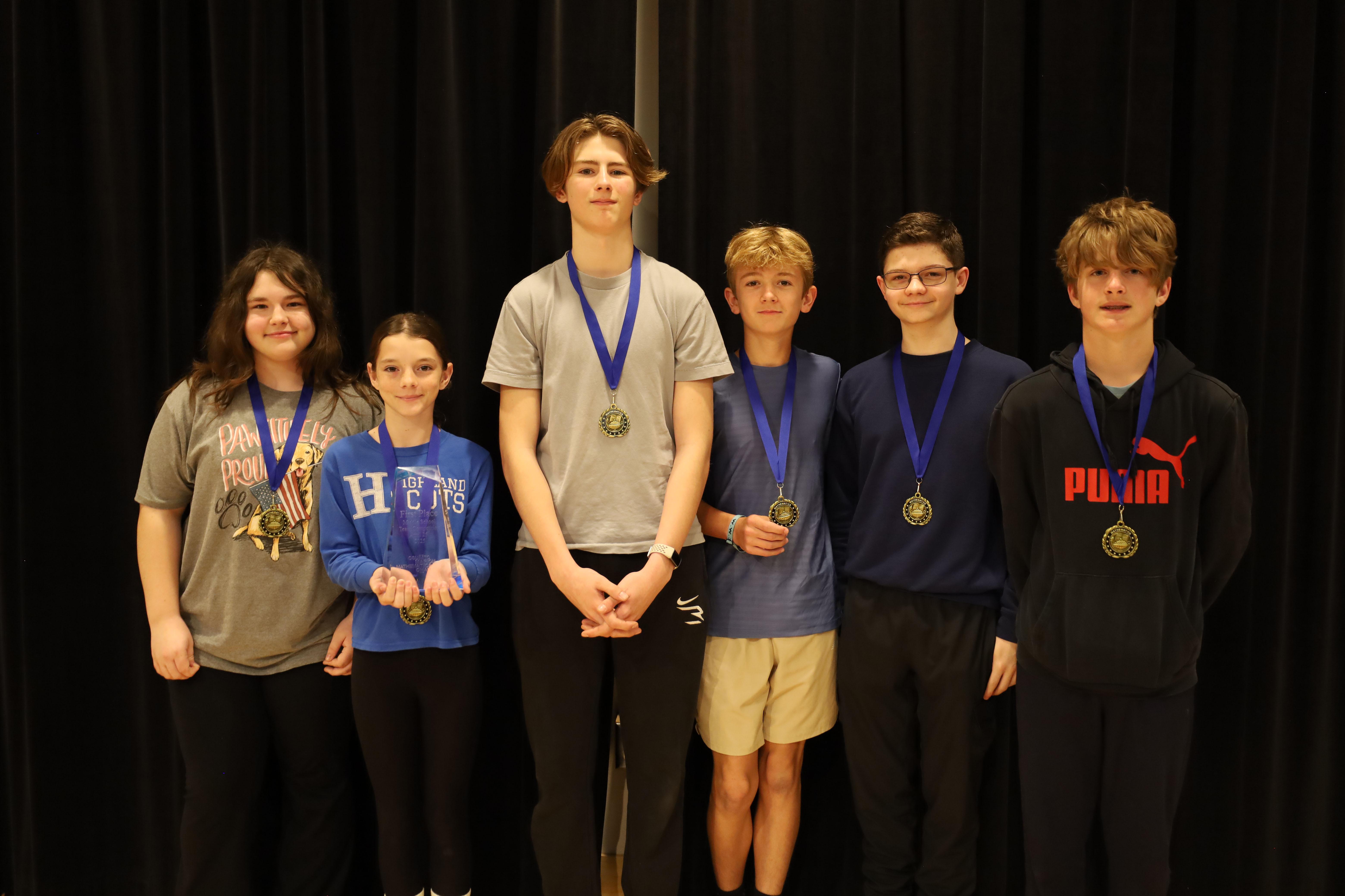six middle school students in front of black curtain wearing medals