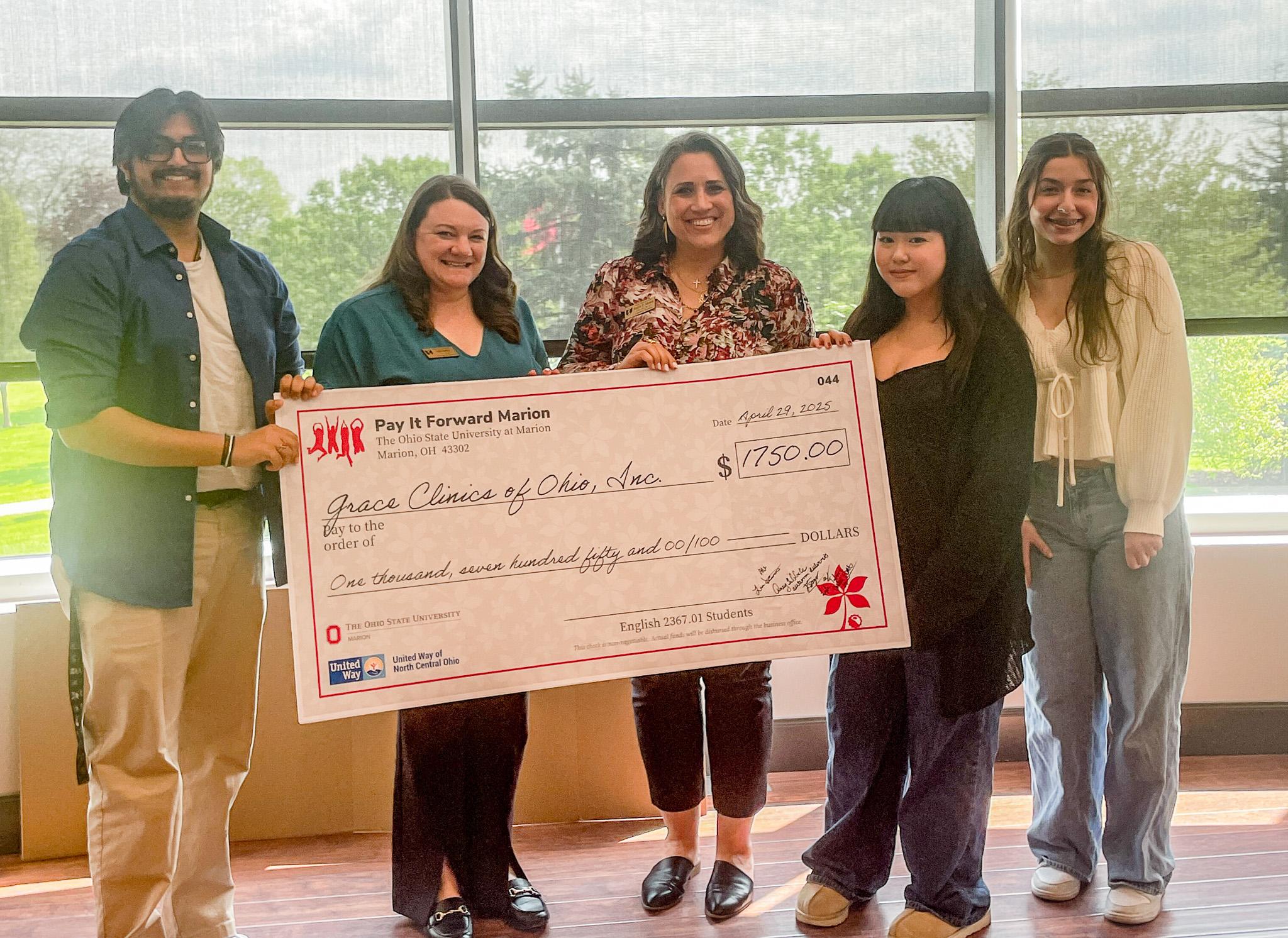 Group of five holding large check in front of windows