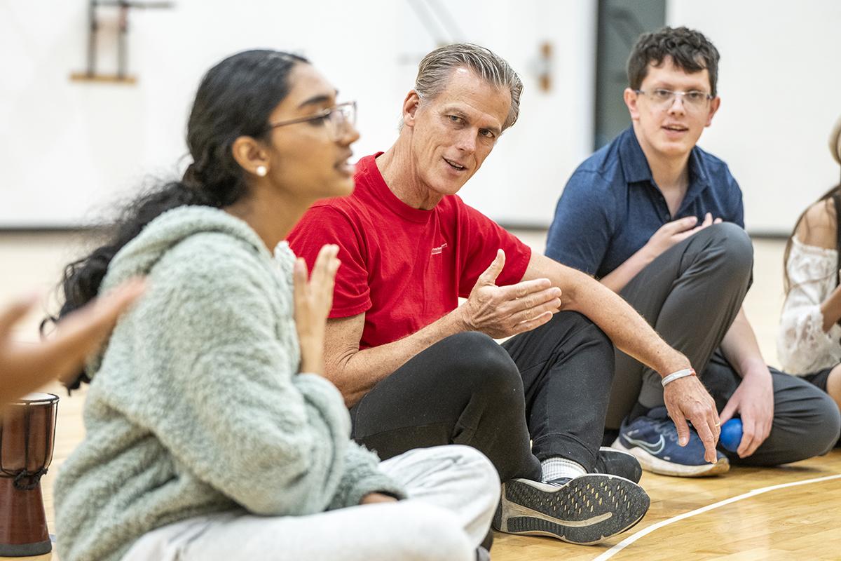 group sitting on gymnasium floor rhythmically tapping body