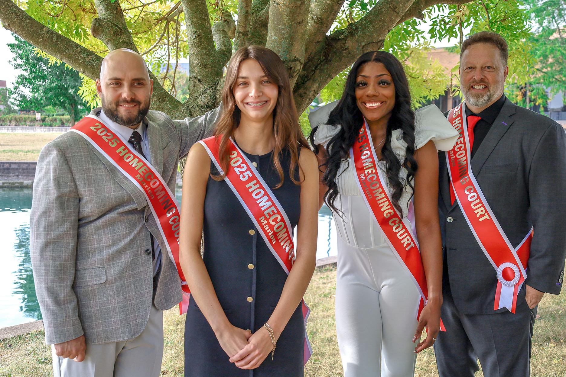 two men and two women under a tree in dress clothes with red sashes