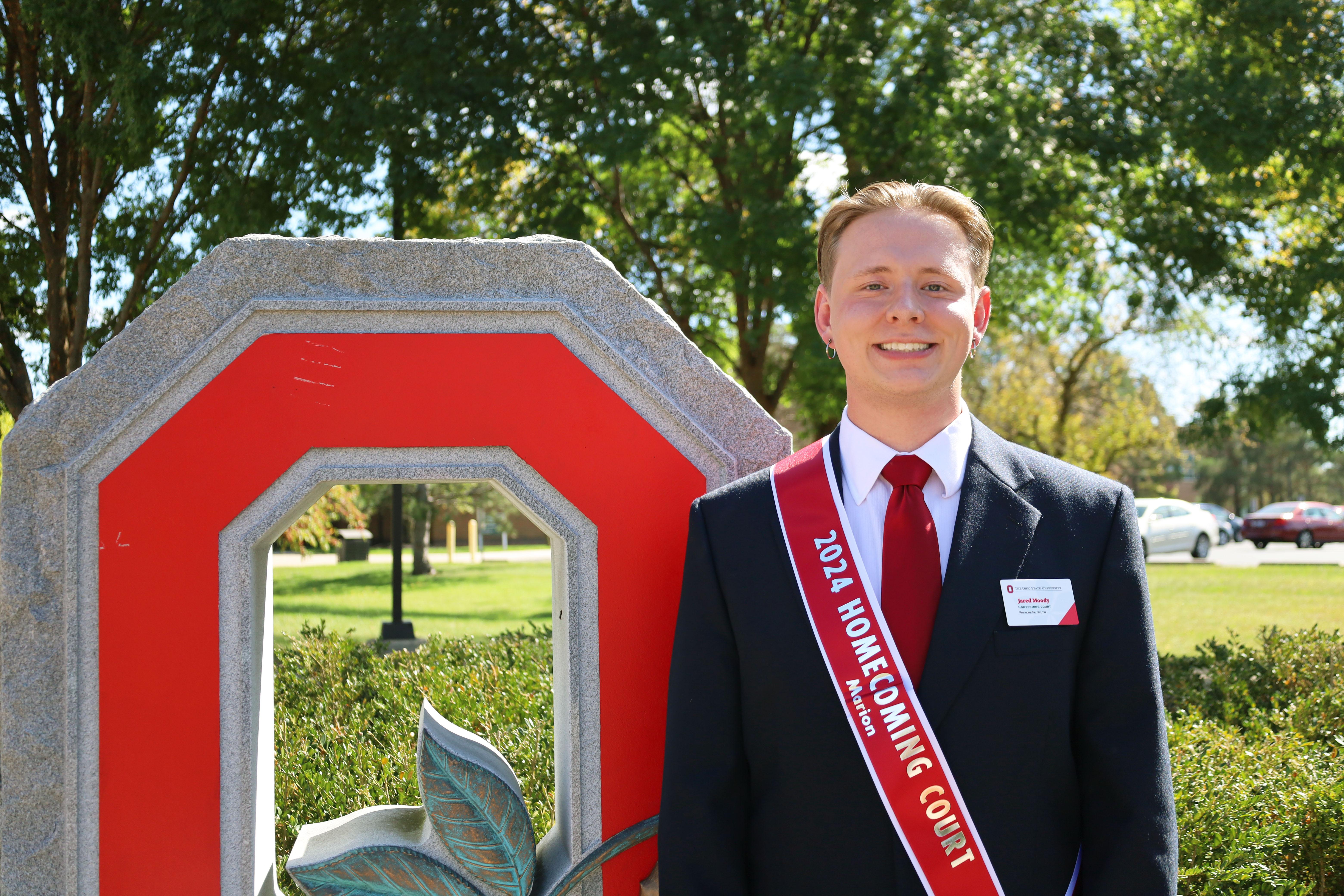 Man in black suit in front of granite block O statue