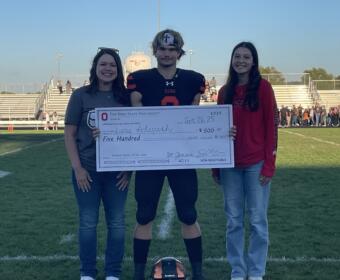 two women present large check to football player mid field