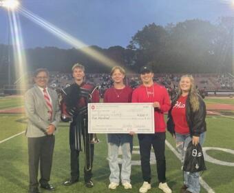 group of five presenting large check on football field at night