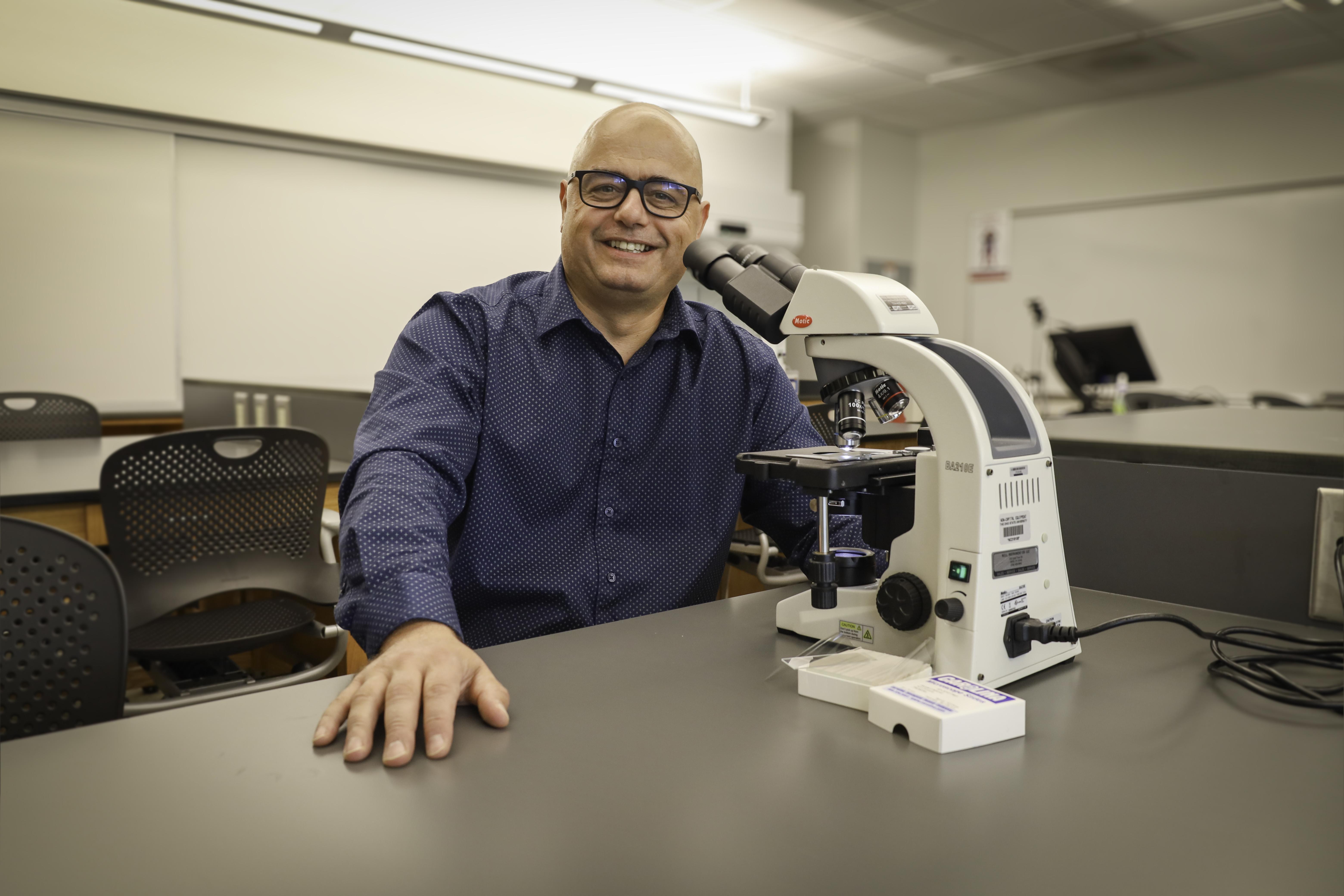 man in classroom lab behind microscope