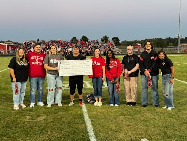 large group presents large check at mid field
