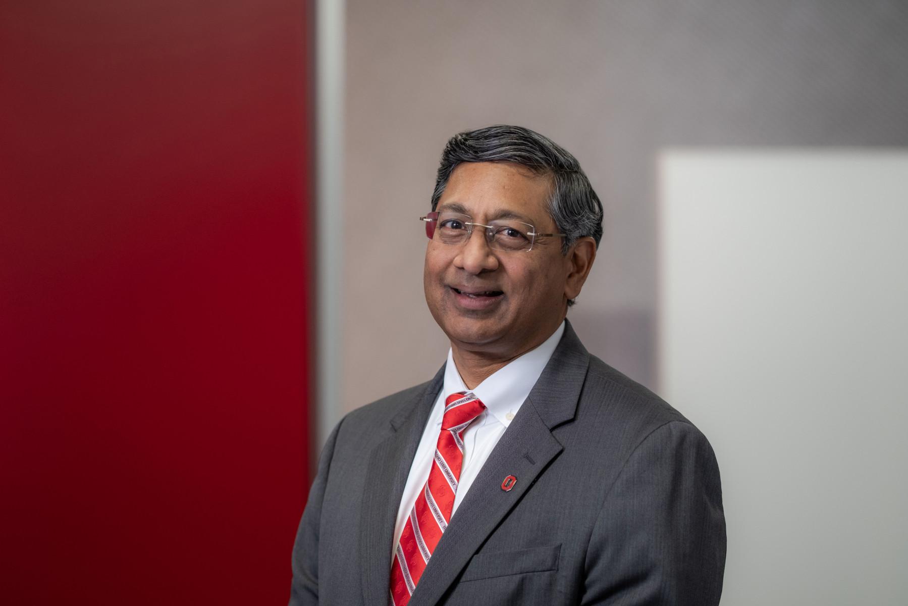 Headshot of man in gray suit and red tie smiling