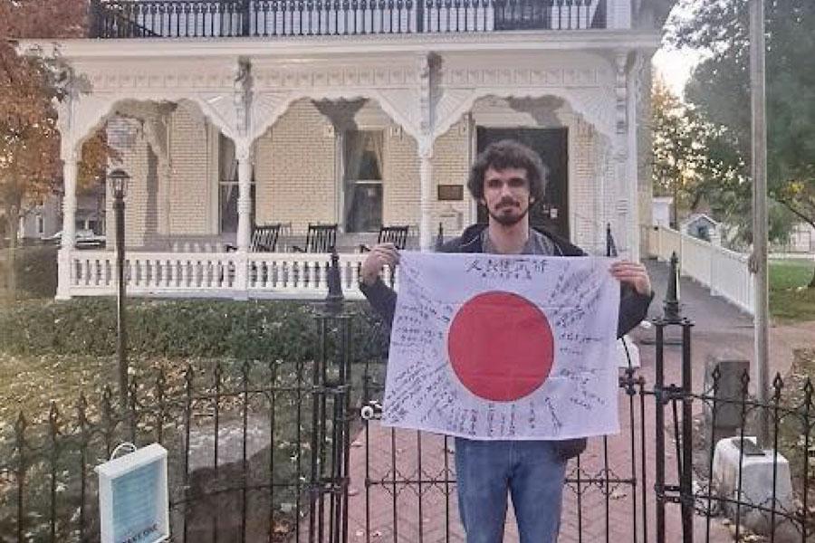 many in front of old colonial home holding Japanese flag