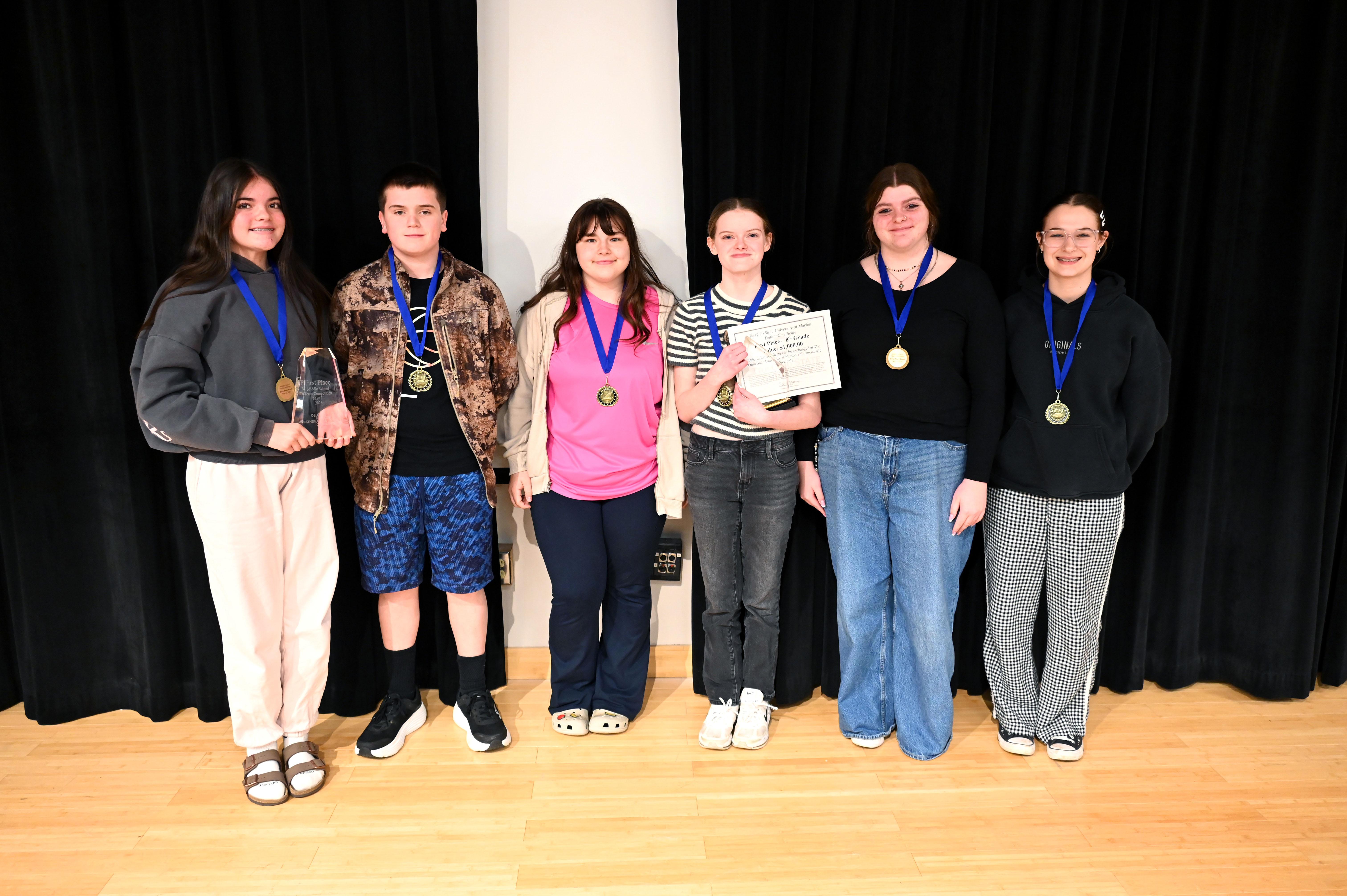 group of six youth holding awards on stage