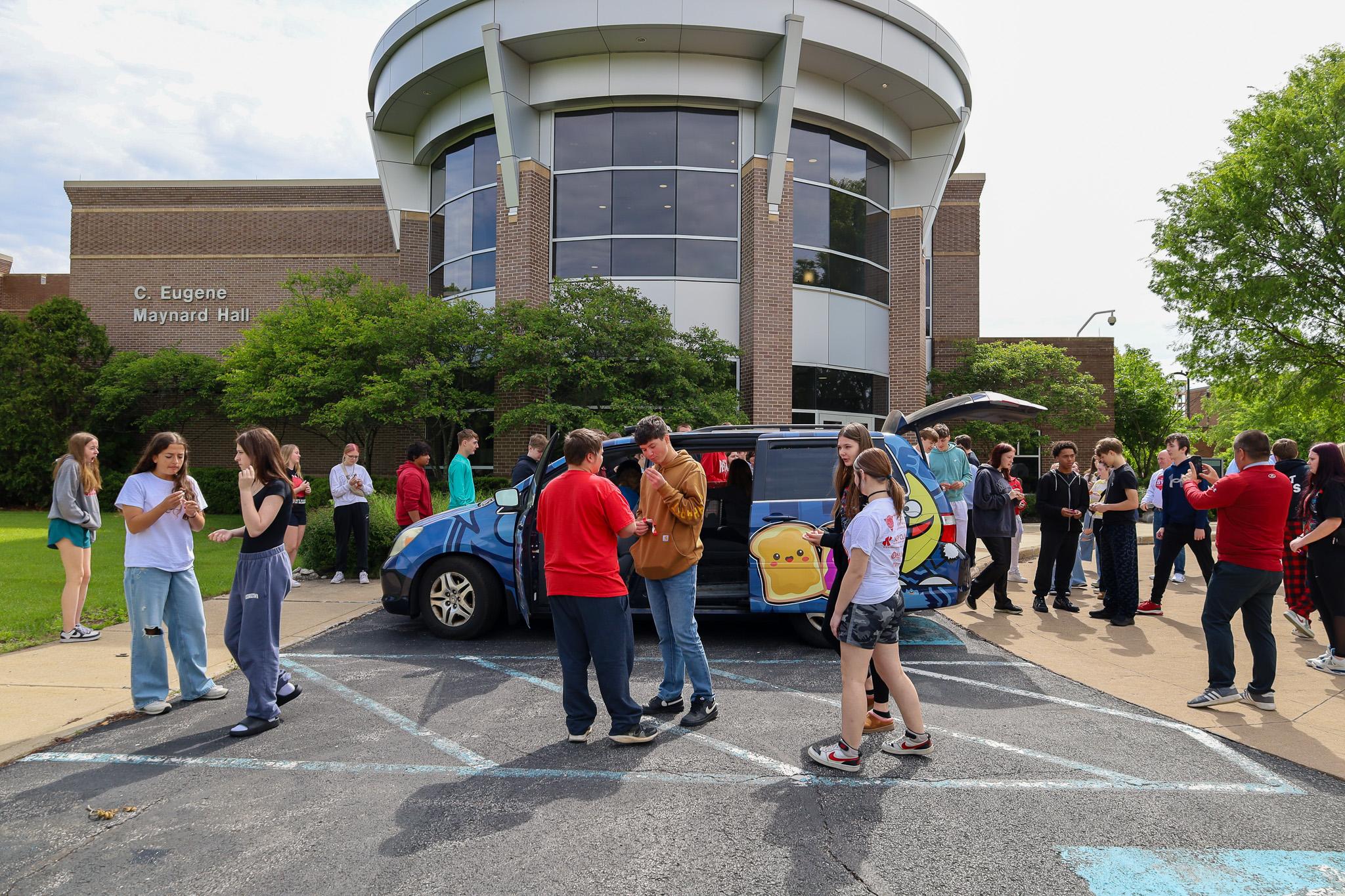 large group of high school students stand outside an academic building surrounding pbj truck