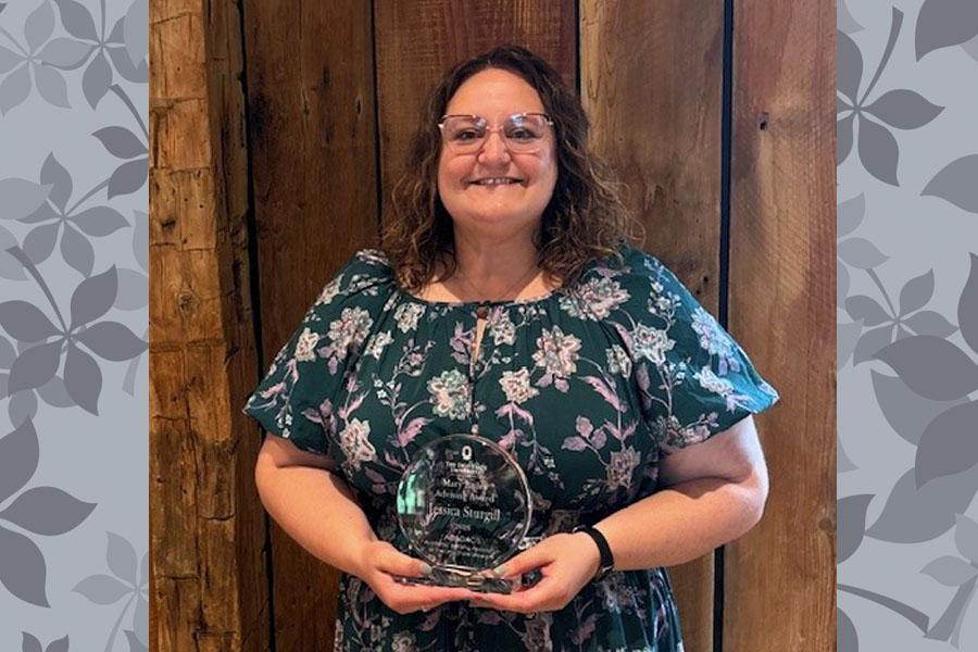 Woman in floral print dress holding acrylic round award and smiling