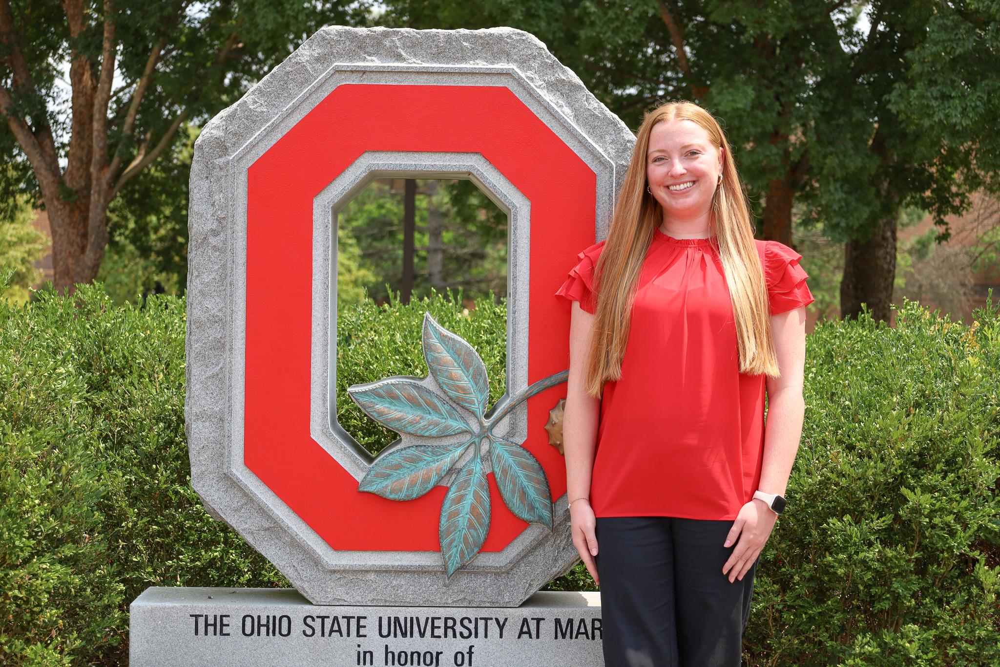 woman in red top standing outdoors next to granite block O monument