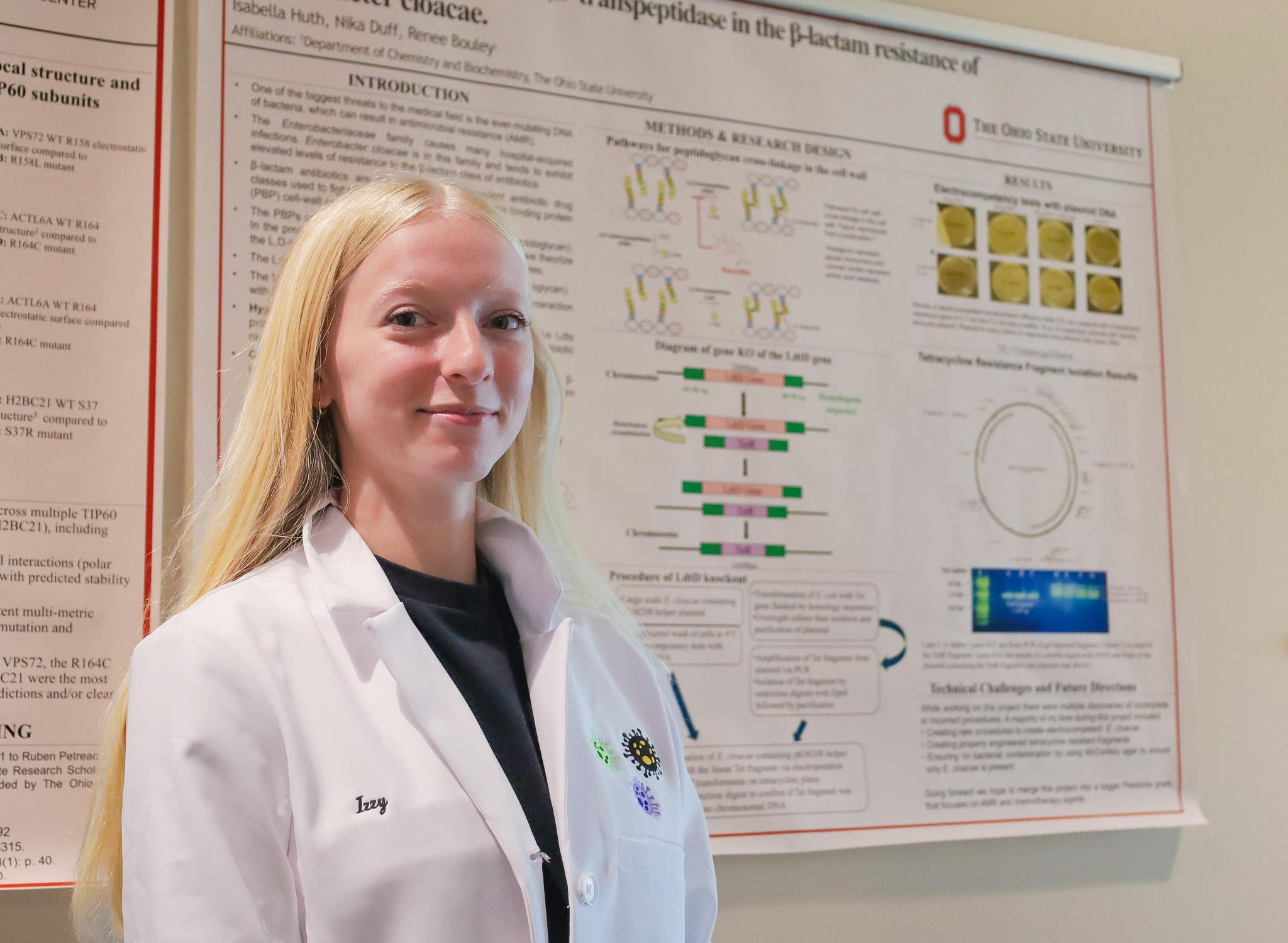 blonde woman in lab coat in front or cancer research poster