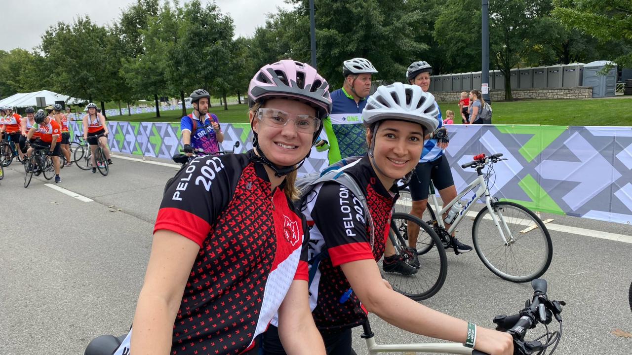 Two women lean bikes over smiling with matching jerseys and helmets