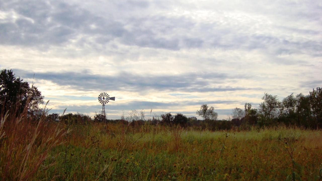 tall grass prairie with a windmill and partly cloudy sky in the background