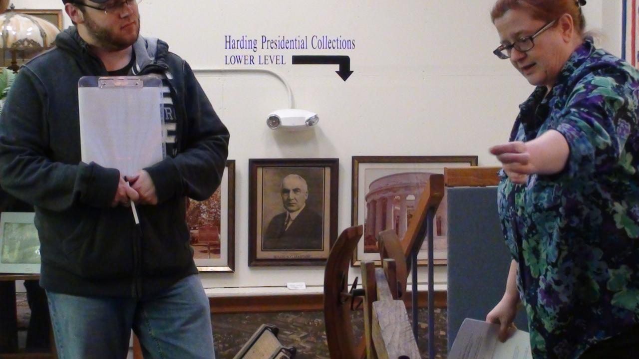 teacher demonstrating turn of the century farm equipment to college student in museum