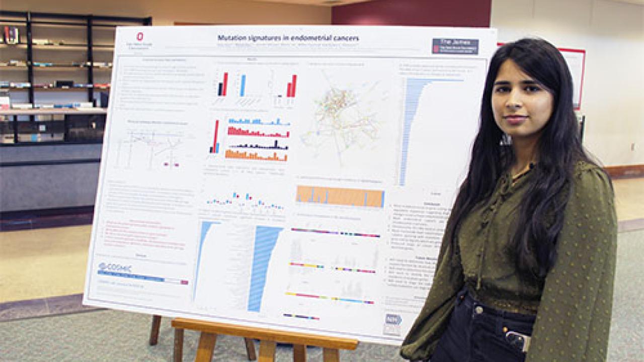 Woman in green shirt standing next to research poster