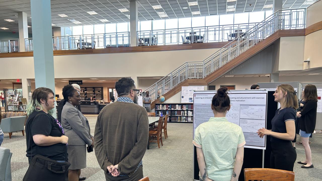 group looks on as college student presents research poster