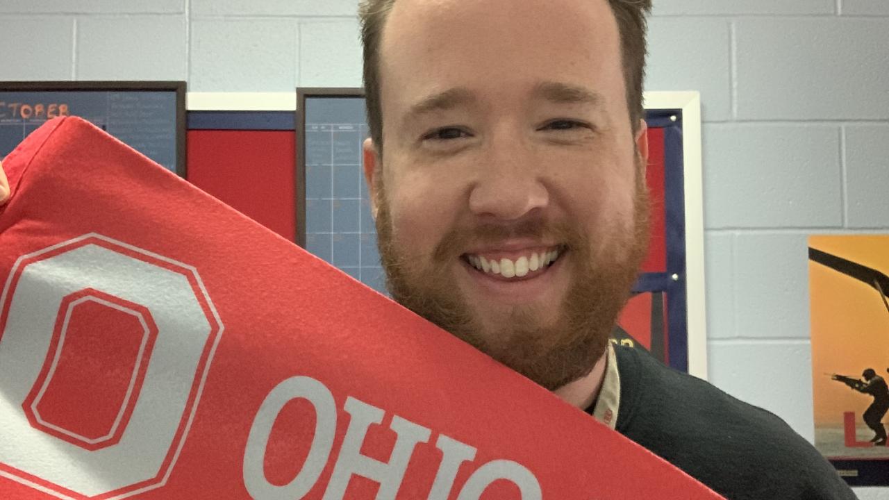 bearded man holding up red college banner