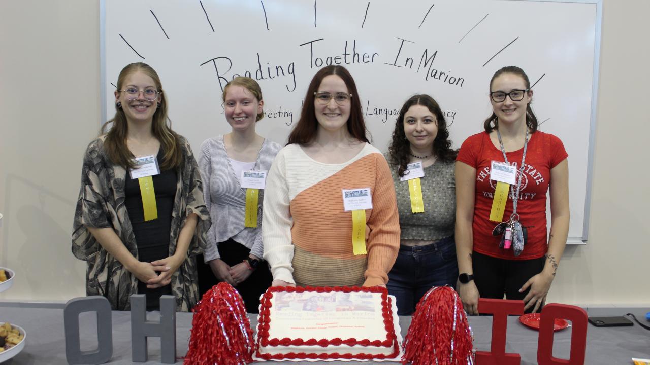 5 college students standing behind a cake