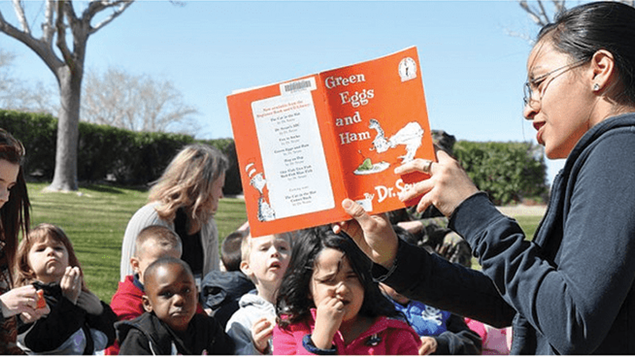 woman reads book to children outside