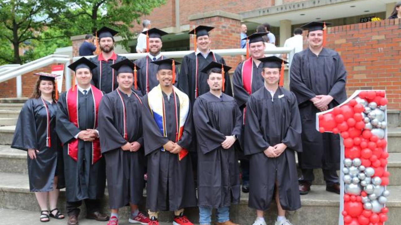 group of college graduates in cap and gown posed on steps