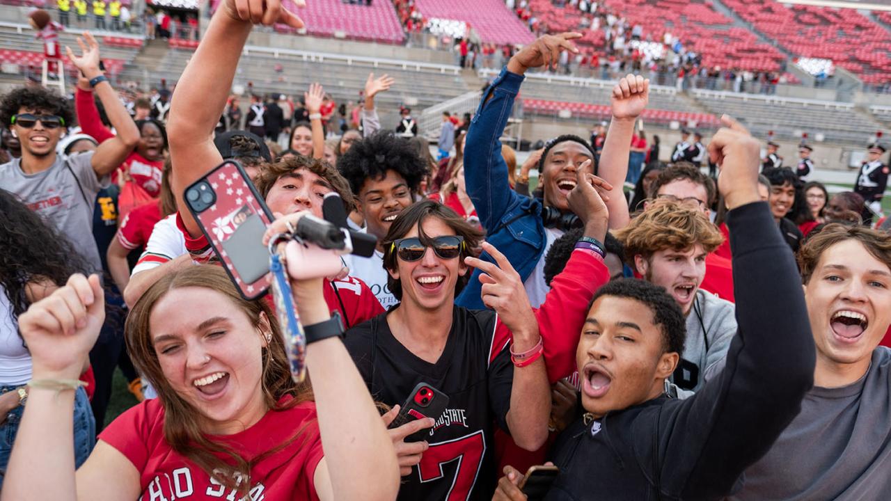 Group of college students in stadium cheering with smart phones in hand