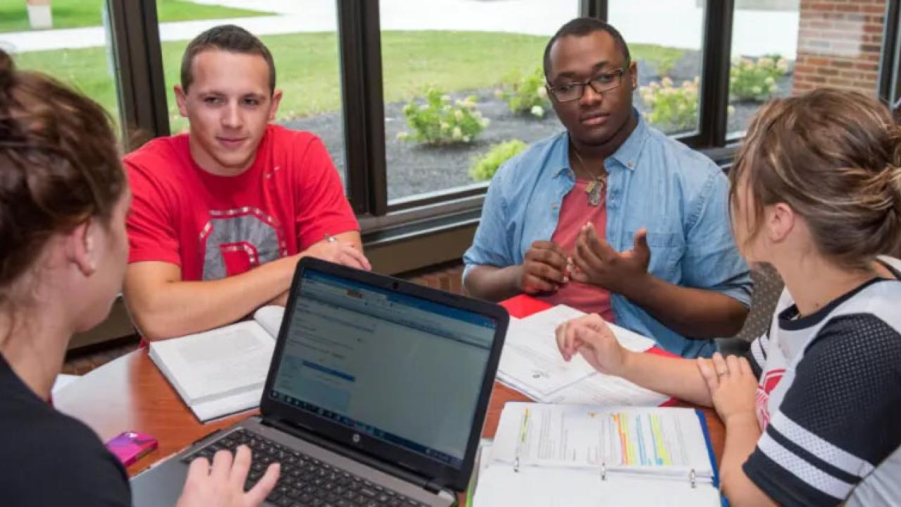 group of four sitting around a computer having discussion