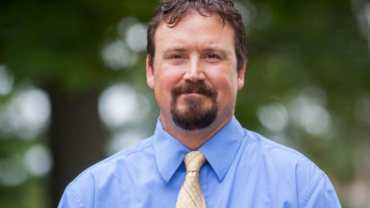man in blue shirt, yellow tie with beard in nature setting