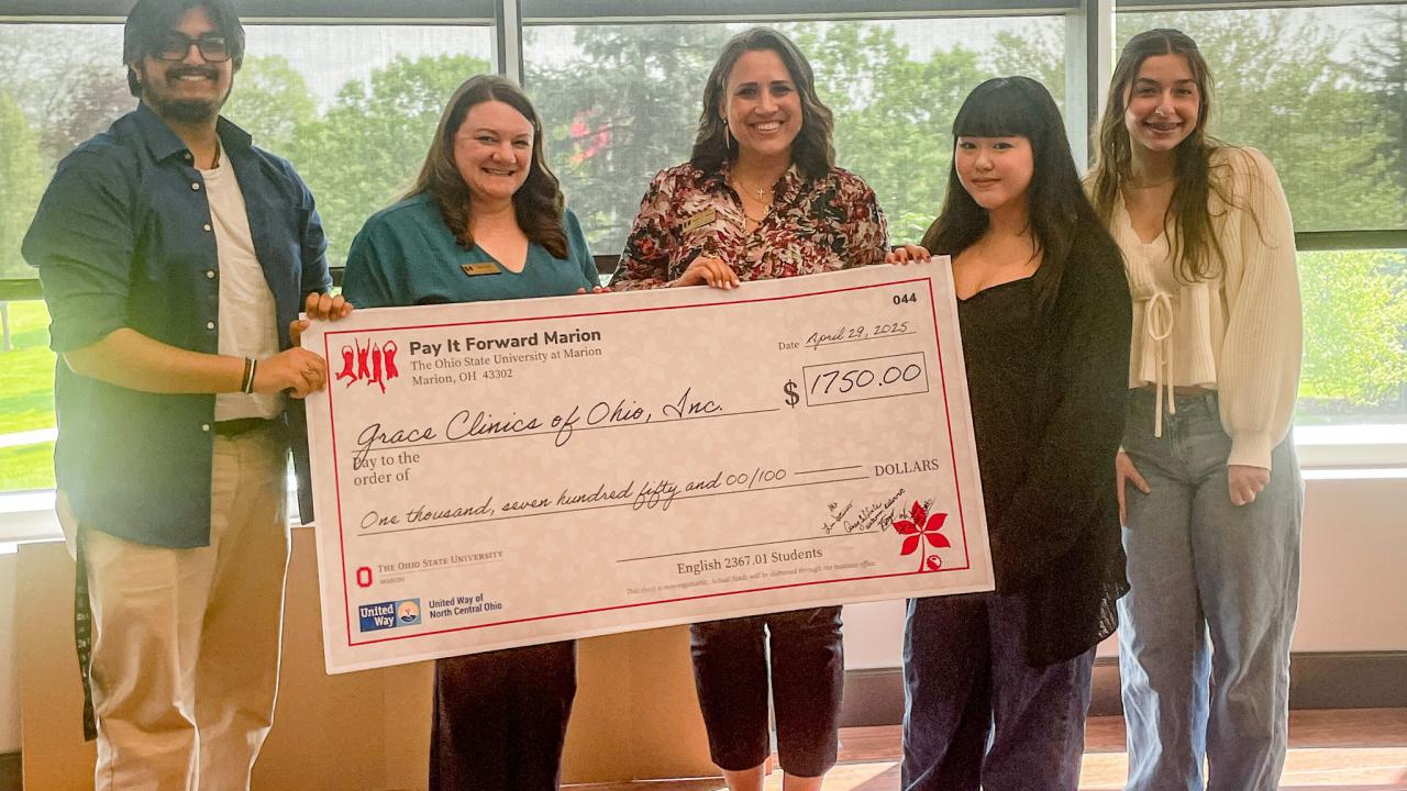 Group of five holding large check in front of windows