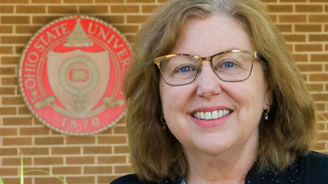 woman smiling with building and university seal in background