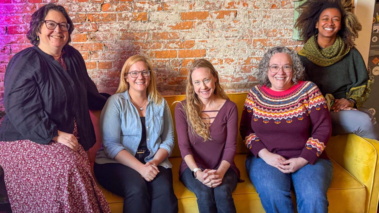 Five women on yellow couch with brick wall behind them
